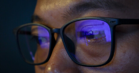 Close up view of focused businessman wears computer glasses for reducing eye strain blurred vision looking at pc screen with computer reflection using internet, reading, watching, working online late. © eza