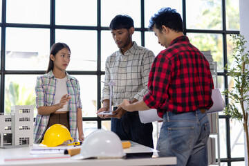 Engineers and architects engaging in a discussion about a wind turbine and building model during a meeting focused on a sustainable construction project, emphasizing renewable energy and innovation.