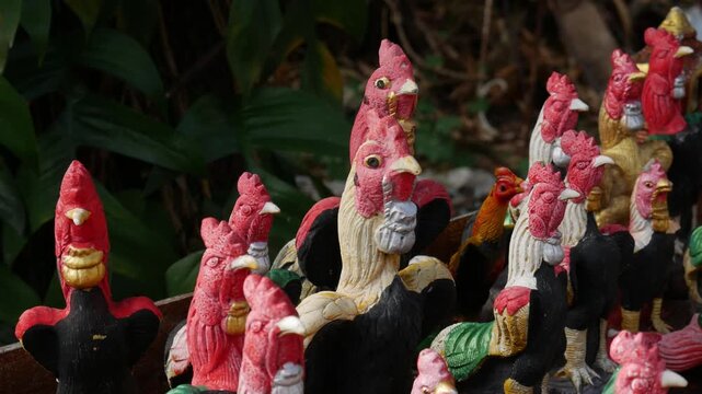 Group of colorful rooster statues as offerings at Thai spirit house or temple shrine, traditional religious belief and superstition concept.