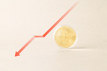 A gold Bitcoin coin sits next to a sharp red downward arrow graph on a neutral background, symbolizing a crypto market crash, financial crisis, price drop, and bearish investment trend.