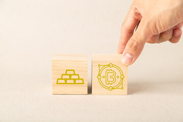 A hand places a wooden block with a Bitcoin icon next to a gold bar icon block, representing financial diversification, investment choice between digital currency and gold, and modern asset management