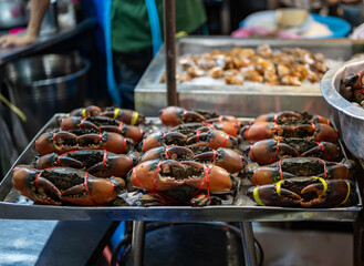 Live crabs stacked on a tray at a Thai street food stall, their claws tied as they wait for sale, capturing the raw and authentic atmosphere of local market life.