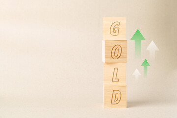Vertical stack of wooden blocks displaying GOLD text with rising green arrows, representing gold price increase, wealth growth, financial stability, and commodity market investment trends.