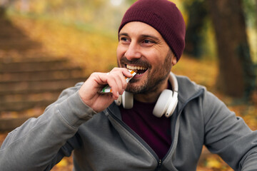 Happy man eating energy bar during autumn workout break