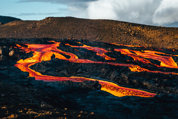 View of molten lava streams carve through the stark, black volcanic landscape under a sky brushed with clouds, Geldingadalir, FAGRADALSFJALL, Reykjanes Peninsula, Iceland.