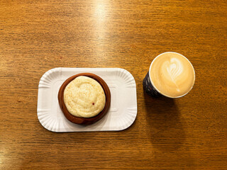 Coffee latte art on wood table with a piece of cake in cafe close-up. Cappuccino with a pattern in a paper cup and cake on a wooden table in a coffee shop top view. The concept of food and drinks.
