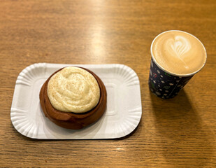 Coffee latte art on wood table with a piece of cake in cafe close-up. Cappuccino with a pattern in a paper cup and cake on a wooden table in a coffee shop top view. The concept of food and drinks.