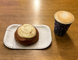 Coffee latte art on wood table with a piece of cake in cafe close-up. Cappuccino with a pattern in a paper cup and cake on a wooden table in a coffee shop top view. The concept of food and drinks.