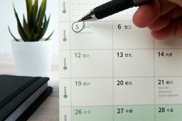 Close up hand holding pen marking Parents’ Day on calendar beside workspace desk. Concept of...