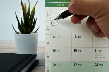 Close up hand holding pen marking Parents’ Day on calendar beside workspace desk. Concept of...