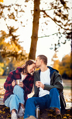 Romantic young multiracial couple enjoying a date in an autumn park, sitting on grass drinking tea.