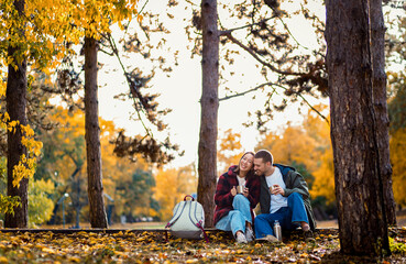 Romantic young multiracial couple enjoying a date in an autumn park, sitting on grass drinking tea.