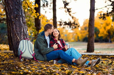Romantic young multiracial couple enjoying a date in an autumn park, sitting on grass drinking tea.