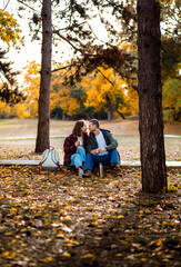 Romantic young multiracial couple enjoying a date in an autumn park, sitting on grass drinking tea.