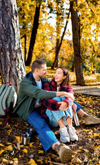 Multiracial couple sitting on grass in autumn park enjoying romantic outdoor date.