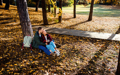 Romantic young multiracial couple enjoying a date in an autumn park, sitting on grass drinking tea.