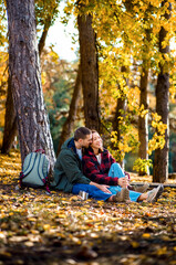 Multiracial couple sitting on grass in autumn park enjoying romantic outdoor date.