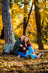 Multiracial couple sitting on grass in autumn park enjoying romantic outdoor date.