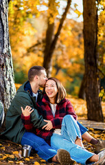 Multiracial couple sitting on grass in autumn park enjoying romantic outdoor date.