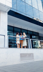 Group of businesswomen standing outside in front of modern office talking.