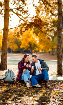 Romantic young multiracial couple enjoying a date in an autumn park, sitting on grass drinking tea.