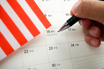 Close up hand holding pen pointing at Malaysia Day on calendar with Malaysian flag. Concept of...