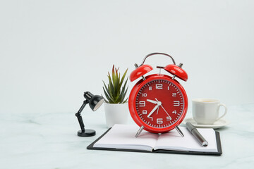 Front view of red alarm clock on open notebook with pen, desk lamp, and coffee cup. Concept of time...