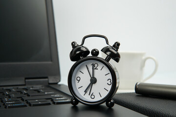 Office workspace with black alarm clock on laptop beside notebook, pen, and coffee cup. Concept of...