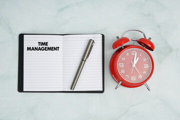 Top view of notebook with time management text, pen, and red alarm clock. Concept of productivity,...