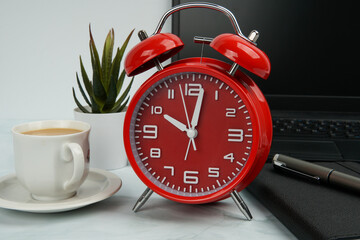 Office workspace with red alarm clock beside laptop, notebook, pen, coffee cup, and plant. Concept...