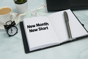 Top view office workspace with open notebook showing “New Month New Start”, pen, alarm clock,...
