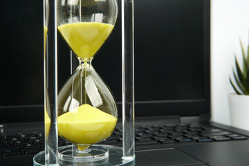 Close up hourglass with yellow sand on laptop keyboard. Concept of time passing, deadline...