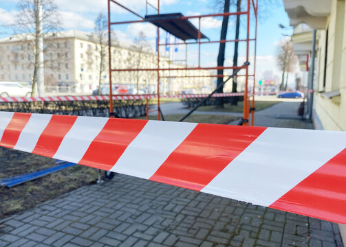 Construction site with red and white caution tape in foreground, scaffolding in background, indicating repair work in a residential city building with copy space
