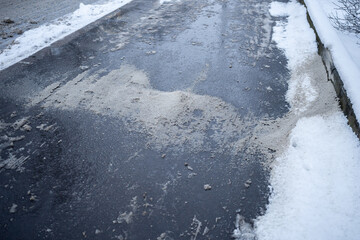 Chemicals for removing ice on snow-covered street in winter. Salt grains on icy sidewalk, asphalt...
