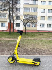 Electric scooter parked on sidewalk with modern building in background, showcasing vibrant yellow color and urban lifestyle concept with copy space