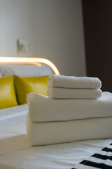 Stack of fresh white bath towels neatly placed on a bed linen. Coziness and clean concept