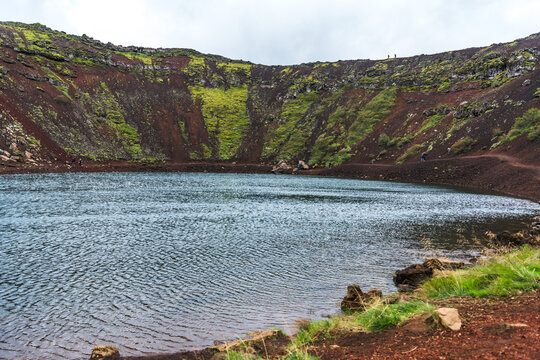View of the Kerid Crater's vivid red slopes descend to meet the serene blue water, creating a stunning contrast of color and texture, Klausturholar, South Iceland, Iceland.