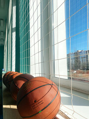 Minsk, Belarus - April 11, 2024: Basketballs lined up on a windowsill in a school gym, showcasing sports education environment with bright sunlight and vibrant colors