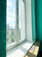 Window with protective netting in a gym, showcasing bright natural light and a vibrant turquoise wall, creating a safe and inviting workout environment