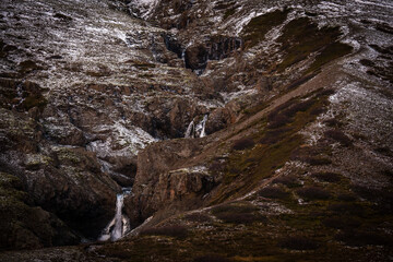 View of a rugged, snow-dusted mountain cascading with icy waterfalls, a stark contrast against the dark, textured rock, Seydisfjordur, East Fjords, Iceland.