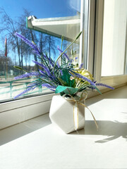 Artificial plant arrangement in a geometric vase on a sunlit window sill, featuring vibrant flowers and greenery, enhancing home decor with a touch of nature