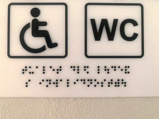Accessible toilet sign featuring Braille and wheelchair symbol, designed for individuals with disabilities, ensuring inclusivity and ease of navigation in public spaces