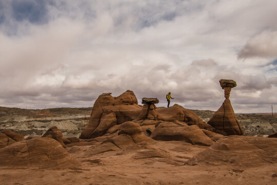 View of a solitary figure stands atop the surreal, mushroom-shaped hoodoos, sculpted by time and weather, against the backdrop of a cloudy sky, Kanab, Utah, Iceland.