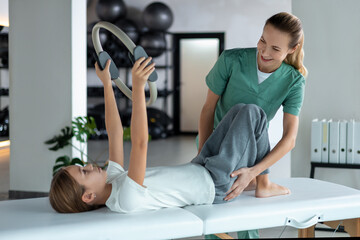 Pediatric physiotherapist assisting girl with Pilates ring exercise