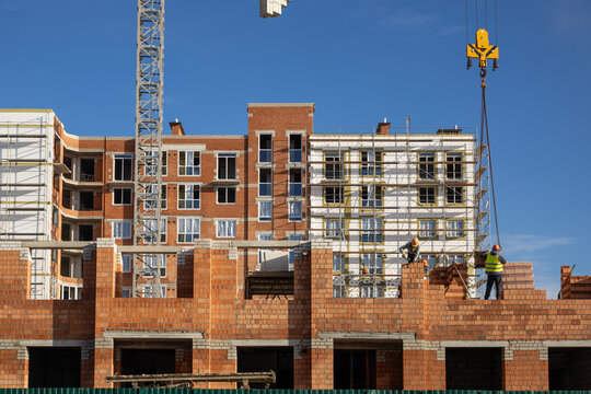 Construction workers building brick apartment house with crane and scaffolding. Multi-story residential building under construction