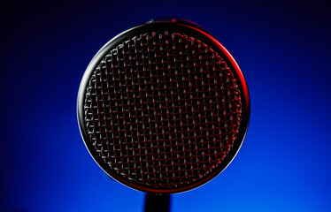 A microphone is shown in detail with a red light highlights part of the mesh. The background is a mix of blue and red light. This setting is typical of a recording studio at night.