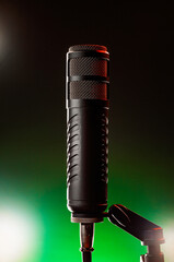 A microphone is placed on a holder in a recording studio. Bright lights in the background create an interesting effect in the room during the evening.