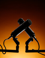 Two microphones are set on a stand, facing each other against a warm orange background. This scene captures a moment in a recording session with equipment ready for use.