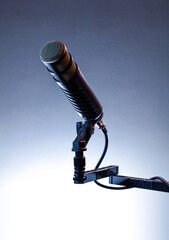 A microphone is mounted on a stand, ready for use in a recording session or speech. The background features simple lighting that emphasizes the microphone's design.