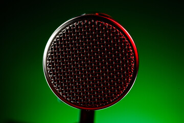 A microphone stands in front of a green backdrop lit by red light. It is ready for use as musicians prepare for their performance. The atmosphere is charged with energy.
